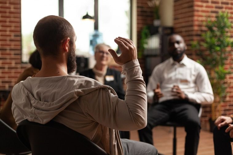 Diverse group of men participating in a supportive therapy session, seated in a circle and engaging in open emotional discussion at a counselling center